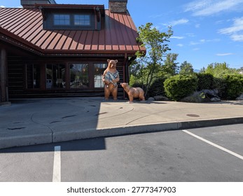 Detailed bear statue featuring two bears and overflowing fish stands near a rustic log cabin surrounded by greenery beneath bright blue Oregon skies.