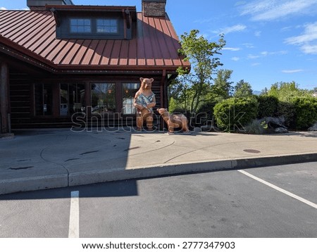 Detailed bear statue featuring two bears and overflowing fish stands near a rustic log cabin surrounded by greenery beneath bright blue Oregon skies.