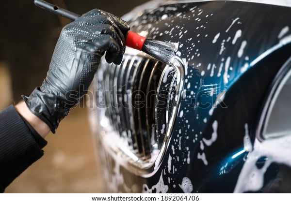 Detailed car wash. Detailing center worker cleans\
car\'s radiator grill with\
brush