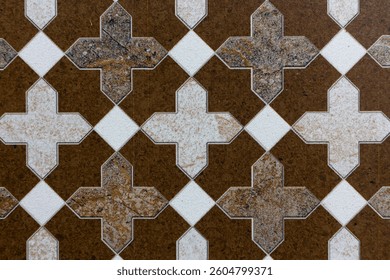 A detailed ceramic tile pattern showcasing a repeating geometric design. The tiles feature a combination of cross-like shapes and diamond patterns, creating a symmetrical and intricate composition.
