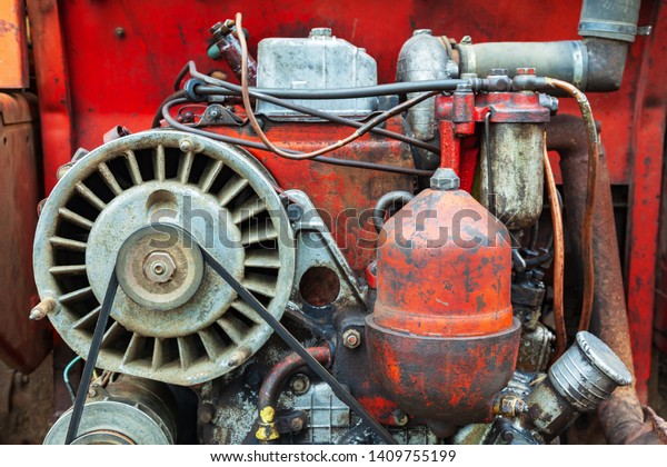 A detailed close up of\
an old messy red vintage tractor engine. Diesel engine air cooling\
soiled in oil and diesel fuel. Parts of the unit agricultural\
machinery.