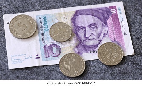 Detailed close-up of 5, 2, and 1 D-Mark coins as well as a 10 D-Mark banknote on gray felt as a background