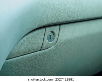 Detailed close-up of a car glove compartment lock on a textured surface. Ideal for automotive articles, manuals, and design inspirations.