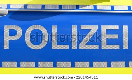 detailed close-up of the lettering POLIZEI in German on the car door of an emergency vehicle in reflective letters between dashed lines on a blue background and a yellow border in the sunlight