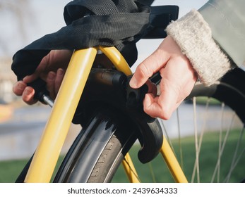 A detailed close-up showing a hand locking the frame of a yellow bicycle, emphasizing the action of securing the bike, with a focus on the lock mechanism and the bike's wheel - Powered by Shutterstock