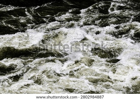 Detailed close-up surface texture of violently churning whitewater rapids on the Jinsha River at Tiger Leaping Gorge, Yunnan Province, China. Raging olive-green currents splinter into an aggressive, multi-directional expanse of boiling white sea-foam and swirling eddies. The full-frame, top-down perspective offers an immersive look at extreme hydrological chaos, capturing the raw, relentless kinetic energy of a legendary wild mountain waterway. Perfect as an organic background representing natural power, turbulence, or unrestrained physical forces.