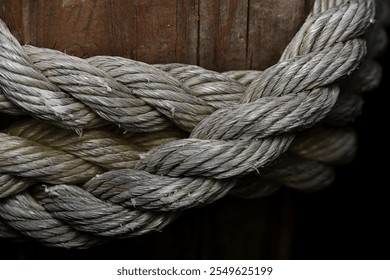 Detailed close-up of a thick, braided rope wrapped around a wooden post. The intricate texture and natural fibers evoke nautical themes, strength, and rustic craftsmanship. - Powered by Shutterstock