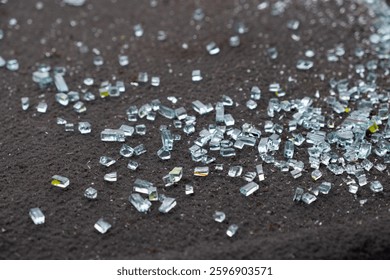 A detailed closeup view of tiny shards of broken glass scattered across a dark, textured surface, effectively capturing the beautiful reflective qualities and shimmering aspects of the glass pieces