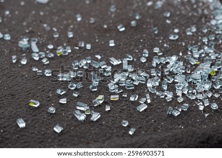 A detailed closeup view of tiny shards of broken glass scattered across a dark, textured surface, effectively capturing the beautiful reflective qualities and shimmering aspects of the glass pieces