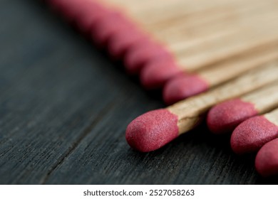 A detailed close-up of wooden matches with red tips arranged on a dark wood surface, showcasing texture and simplicity in a still life composition. - Powered by Shutterstock