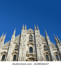 Detailed frontal view of Milan Cathedral’s stunning Gothic architecture, with sharp spires and elaborate stone carvings set against a vivid blue sky. - Powered by Shutterstock - Get 15% off with code: PIKWIZARD15