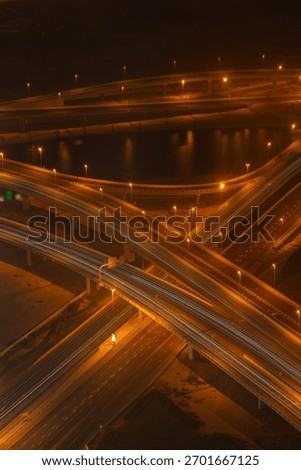 A detailed high-angle view of a complex highway intersection at night, captured using long exposure to create bright light trails