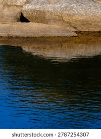 Detailed horizontal view of solid rock strata sharply contrasting with a rippling dark blue water surface.