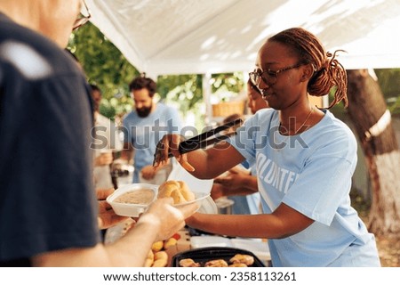 Detailed image of black woman at a food drive sharing free warm meals to poor caucasian homeless person. At local center group of volunteers feed and support the hungry and underprivileged.