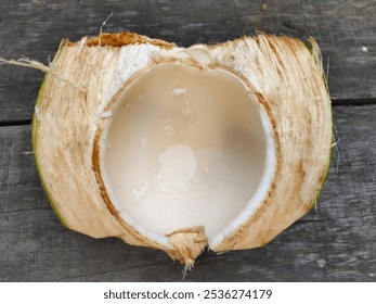 A detailed image of a halved coconut showcasing fresh coconut water and fleshy interior. Set against a rustic wooden background, highlighting the natural texture and freshness. - Powered by Shutterstock