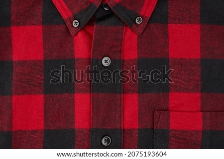 Detailed photograph of a men's flannel shirt in a tartan pattern, showing a portion of the collar and pocket with the centerline and buttons