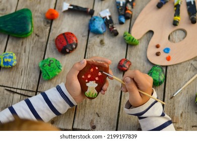 A detailed picture of a child's hands drawing a fungus on a stone with acrylic paints. Home hobbies are authentic. Artwork on stones. - Powered by Shutterstock