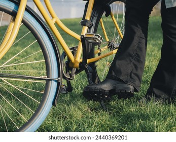 A detailed shot captures a person's foot lifting the kickstand of a yellow bicycle, preparing to ride off on a grassy field