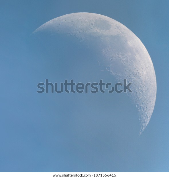 Detailed shot of crescent moon in a pale blue\
sky. Craters cast expressive\
shadows.