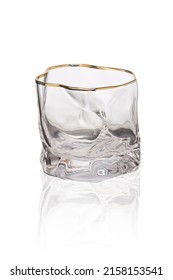 Detailed shot of a glass in the form of a spherical ice. The designer transparent asymmetrical glass with a thick bottom and a golden border is isolated on the white background.