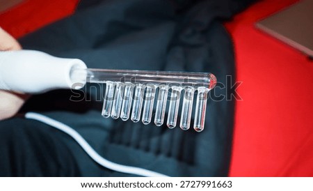 Detailed shot of glass rake attachment on white handle, grasped by hand against red and dark background fabrics.