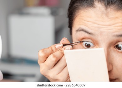 detailed shot of a latina woman using a manual eyebrow tweezer to apply false eyelashes - Powered by Shutterstock