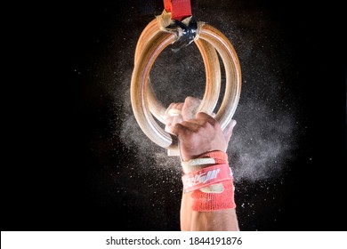 Detailed shot of male gymnast catching gymnastic rings with chalk dust on black background.