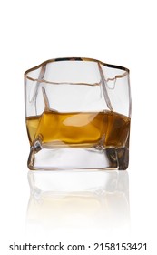 Detailed shot of a spherical ice glass with whiskey. The designer transparent asymmetrical glass with a thick bottom and a golden border is isolated on the white background.
