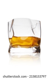 Detailed shot of a spherical ice glass with whiskey. The designer transparent asymmetrical glass with a thick bottom is isolated on the white background.