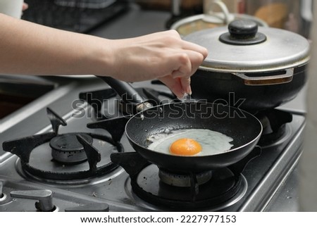 detailed shot of a woman's hand adding salt to the egg she is frying in a frying pan on the burner of a gas stove in a Colombian kitchen.