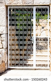 a detailed squiggle patterned white gate with a old stone wall