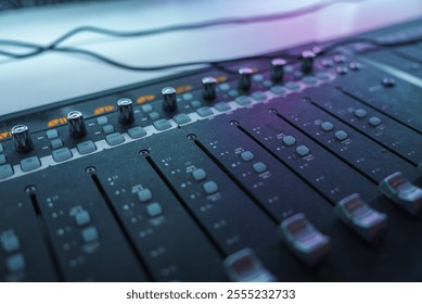 A detailed view of an audio mixing console with sliders and knobs, illuminated by ambient lighting. The setup suggests a modern recording studio environment. - Powered by Shutterstock