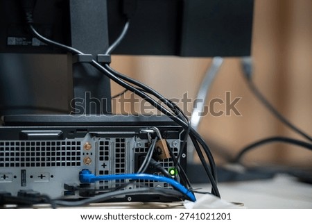 A detailed view of the backside of a computer workstation, showcasing the complex arrangement of cables and connections for various devices. Ideal for technology-related content.