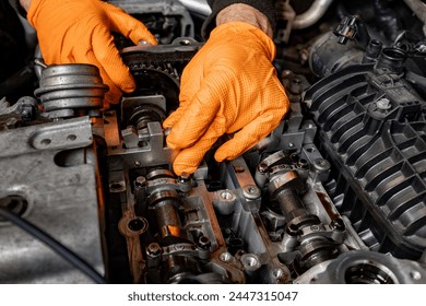 Detailed view of a car mechanic's hands, protected by orange gloves, as they attentively work on repairing an opened car engine in an auto service - Powered by Shutterstock