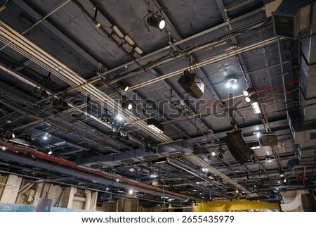 Detailed view of the ceiling inside the Intrepid Museum showing lighting equipment, pipes, and speakers. The exposed industrial infrastructure supports sound and light systems for exhibits and