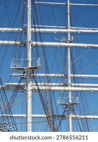 Detailed view of the complex rigging and white masts of a historic tall ship against a clear blue sky.
