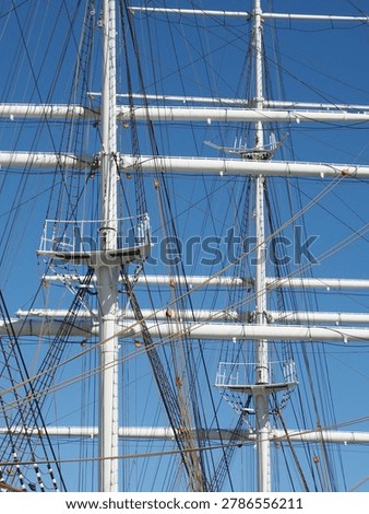 Detailed view of the complex rigging and white masts of a historic tall ship against a clear blue sky.