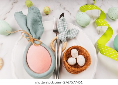 Detailed view of Easter setting with linen bunny napkin, pink egg, silverware and nest with speckled eggs on a white ceramic plate