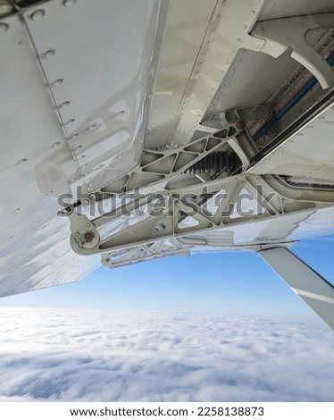 Detailed view of flaps , high-lift devices and actuators of a general aviation airplane flying at stall speed. Strut and wing of semi-cantilever high-wing aircraft over the clouds on a sunny day.
