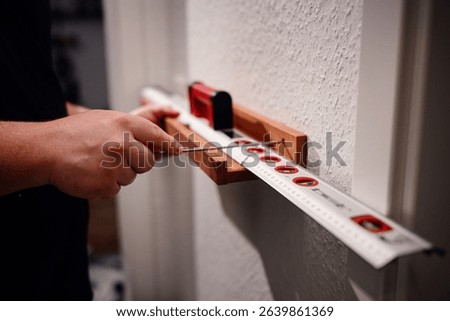 Detailed view of hands using a screwdriver and spirit level to align and secure a wooden bracket onto a white wall.