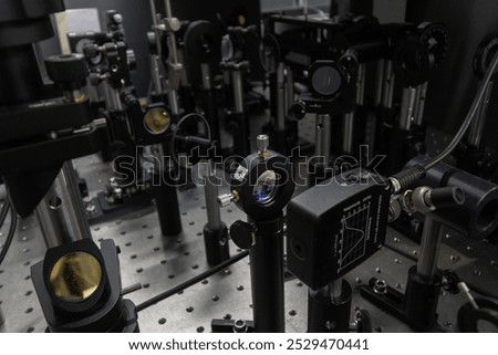 A detailed view of a high-tech optical lab setup featuring various mounted lenses, mirrors, and sensors for laser and photonics experiments. Precision and control mechanisms are prominently displayed