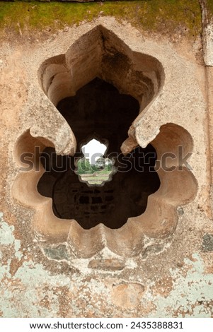 A detailed view of an intricately carved ancient stone window in an old, weathered wall with natural light passing through, reflecting historical architecture at ahaz Mahal, Mandu, India.