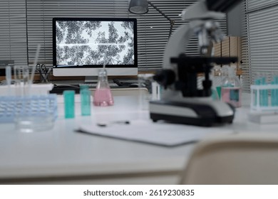 Detailed view of a laboratory setup with a microscope and computer analyzing specimens. Various laboratory equipment and chemicals are visible on countertops