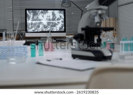 Detailed view of a laboratory setup with a microscope and computer analyzing specimens. Various laboratory equipment and chemicals are visible on countertops