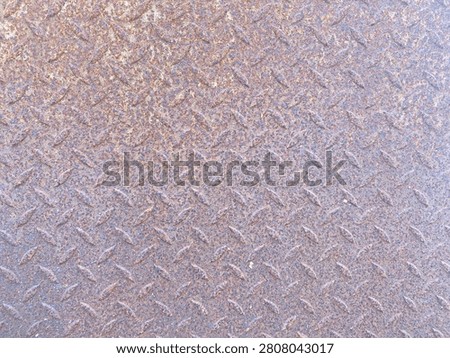 A detailed view of a metal surface featuring a raised diamond pattern, showing subtle variations in color and light reflection