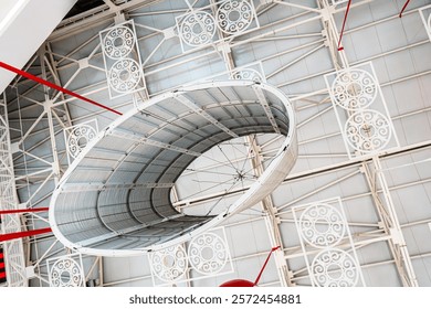 A detailed view of a modern ceiling structure featuring an intricate arrangement of metal beams, circular patterns, and a large central installation. The design showcases symmetry and innovation