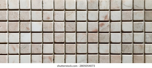 A detailed view of a mosaic pattern featuring small, square tiles in various shades of beige and white, creating a textured surface.