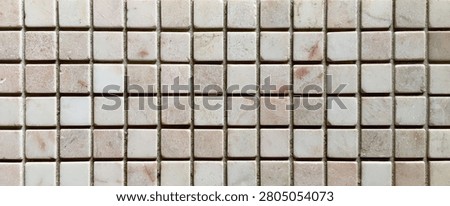 A detailed view of a mosaic pattern featuring small, square tiles in various shades of beige and white, creating a textured surface.