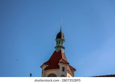 A detailed view of an old lighthouse structure featuring a distinctive red tiled roof and a tall spire reaching towards the bright sky