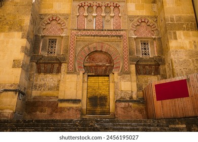 A detailed view of an ornate archway at the historical site in Cordoba, featuring intricate Islamic architecture with carved stone, decorative tiles, and a striking golden door. - Powered by Shutterstock